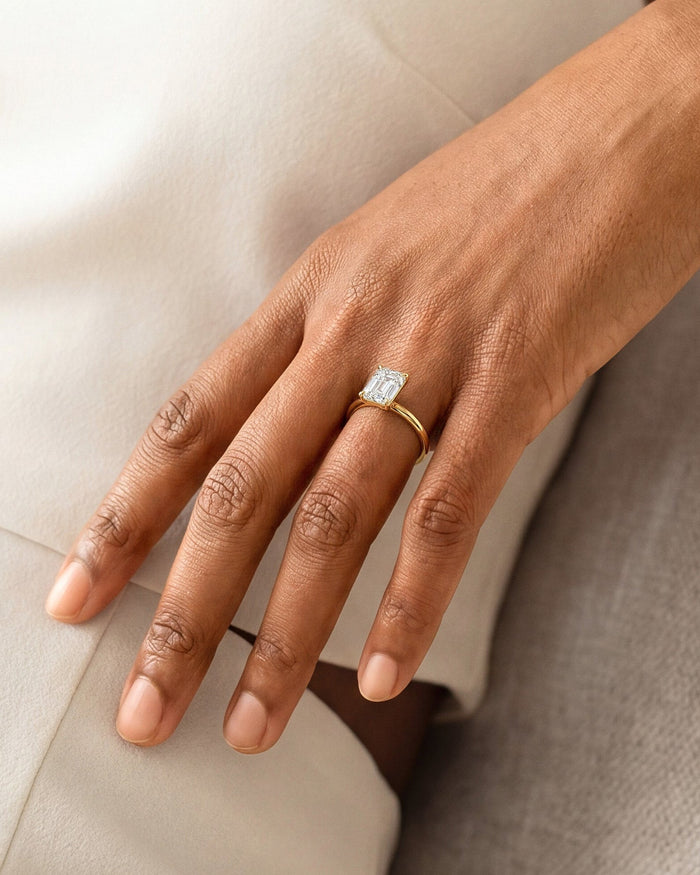 Emerald cut lab grown diamond plain band ring in yellow gold on a relaxed hand against beige fabric