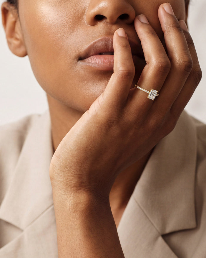 Emerald cut lab grown diamond pave engagement ring in white gold worn on the hand at the lips