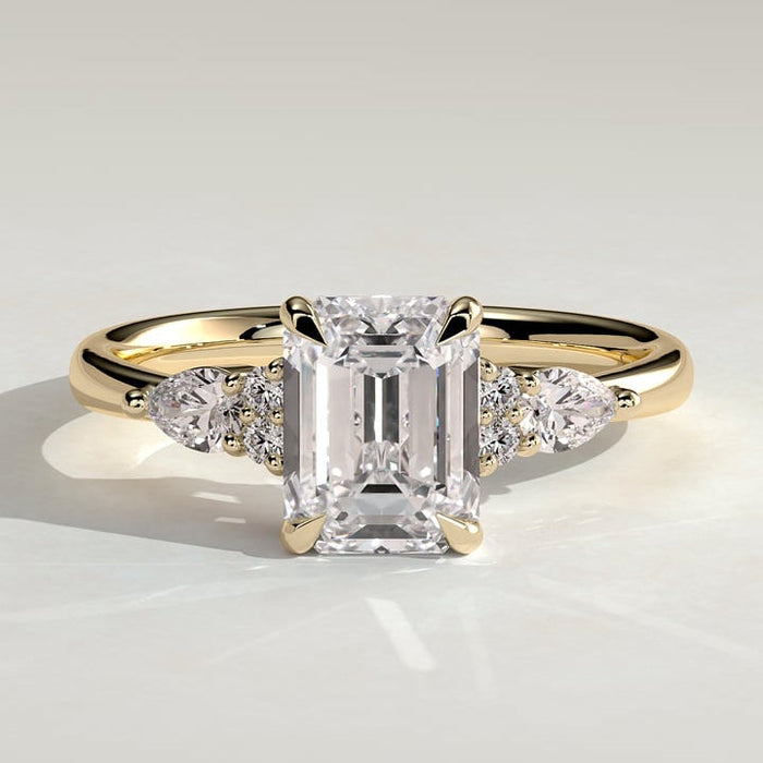 Emerald cut moissanite engagement ring with pear and round cluster shoulders in yellow gold