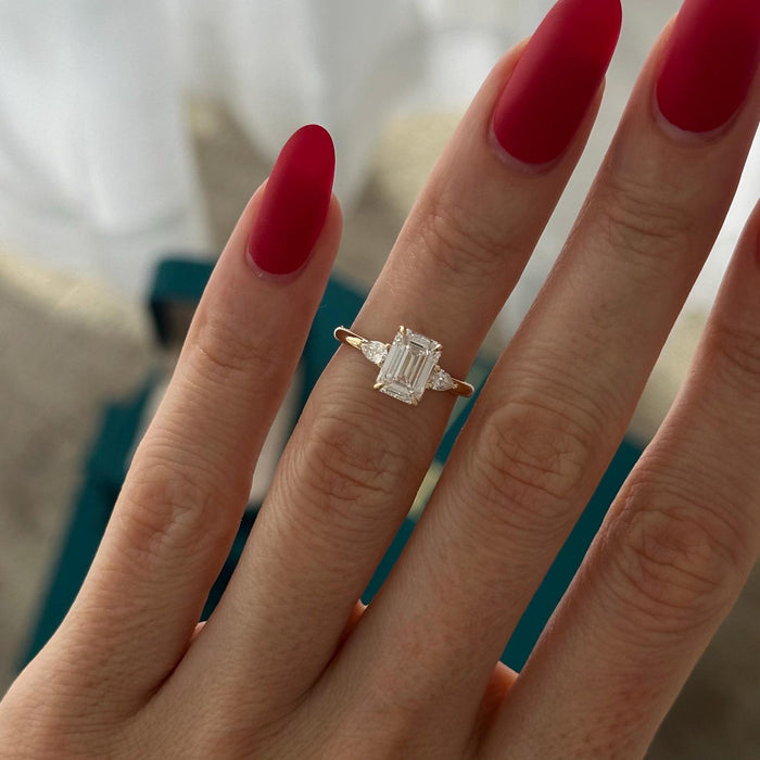 Emerald cut moissanite petite three stone engagement ring with pear side stones in yellow gold, view 2