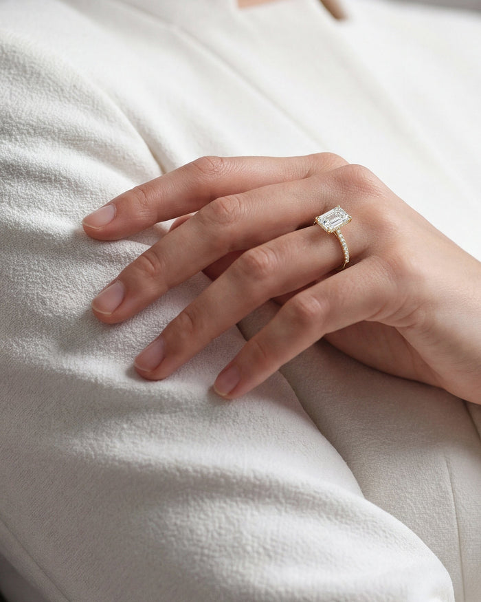 Large emerald cut lab grown diamond pave ring in yellow gold worn on the hand resting on a white coat