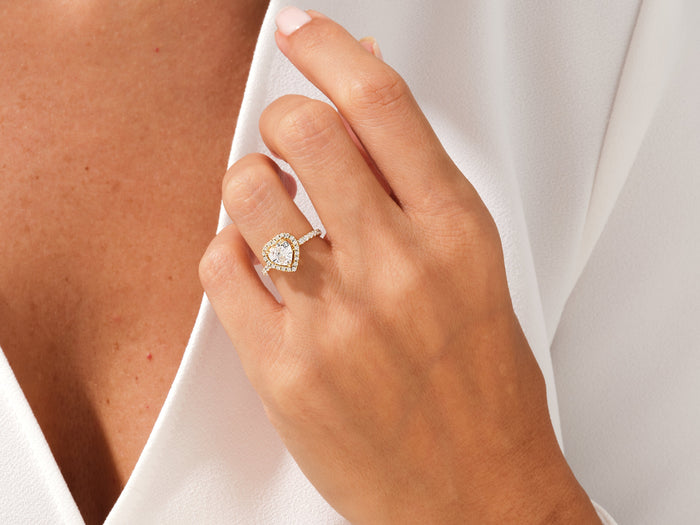 Heart moissanite halo ring in yellow gold worn on the hand, fingers resting on the collarbone