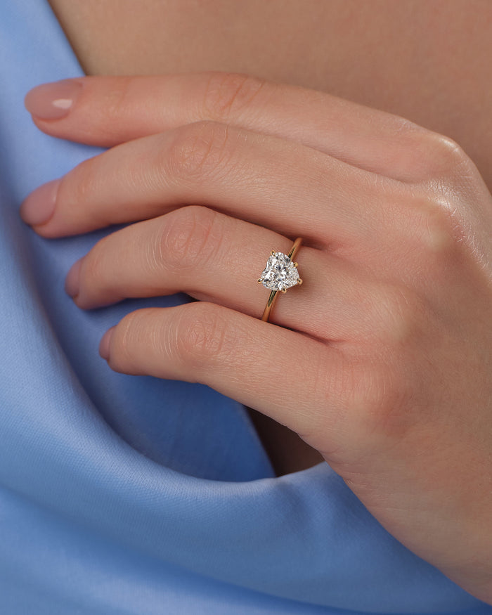 Heart shaped lab grown diamond solitaire ring worn on the hand against blue fabric