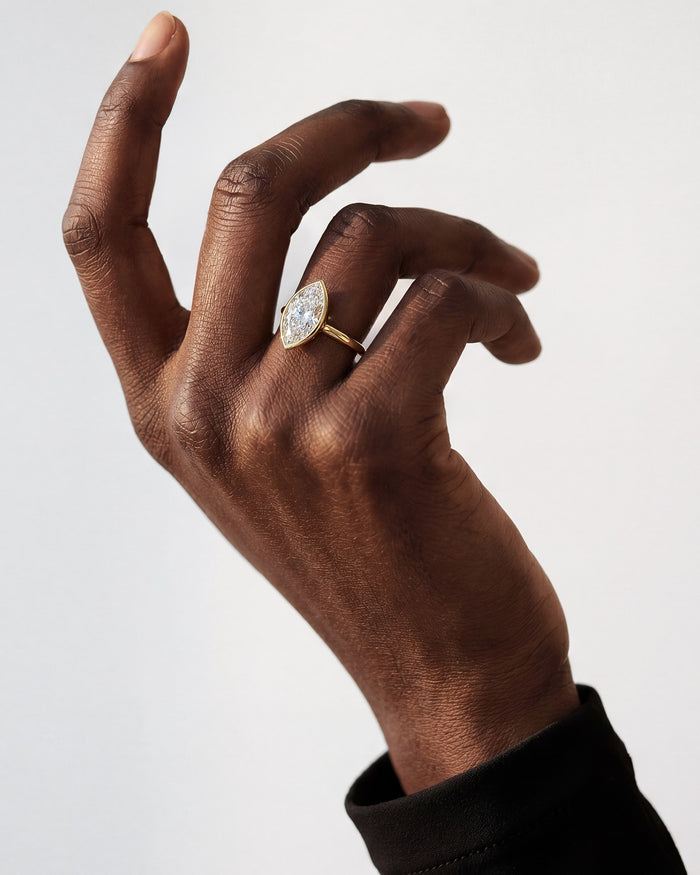 Large marquise lab grown diamond bezel ring in yellow gold on a raised hand, fingers curled