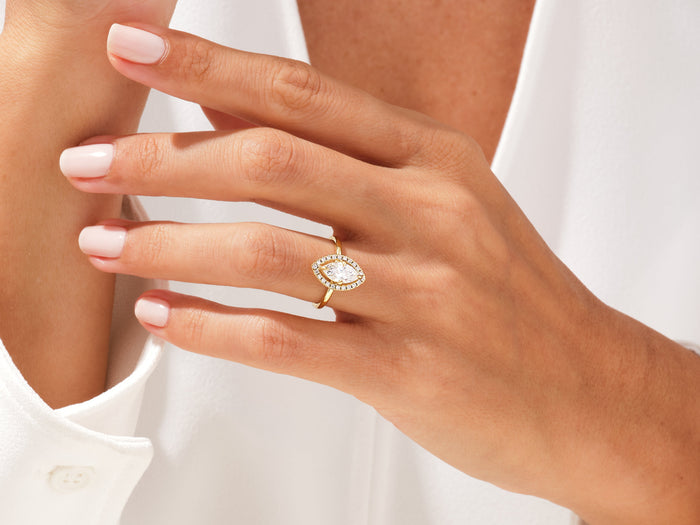 Marquise lab grown diamond pave halo engagement ring worn on the hand held at the chest