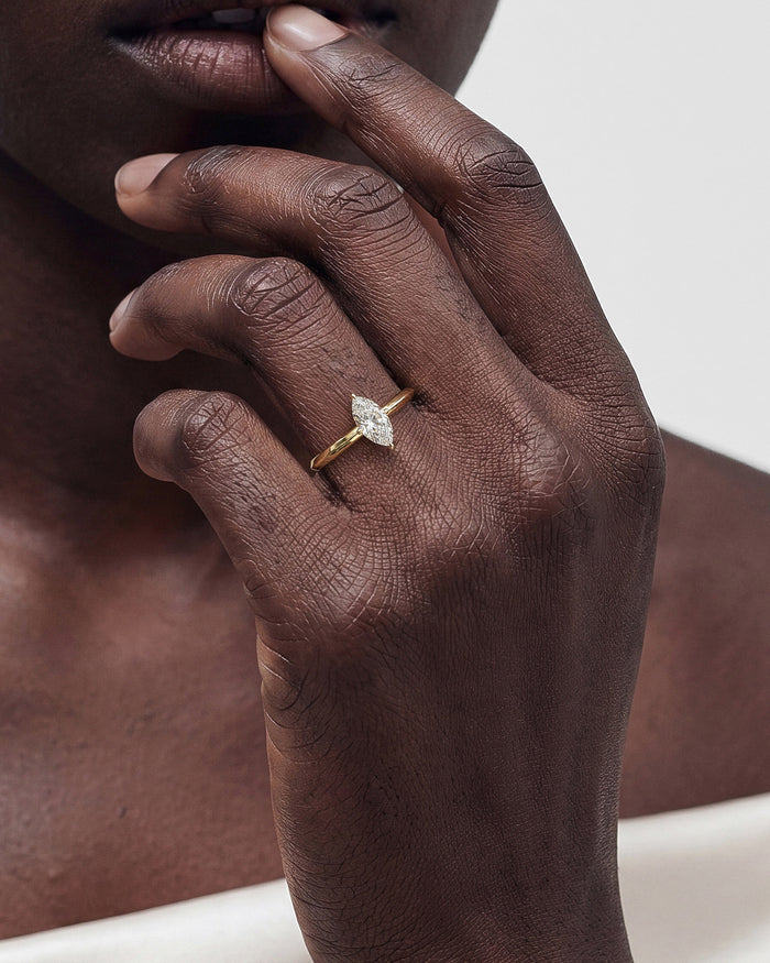 Dainty marquise lab grown diamond knife edge ring in yellow gold worn on a hand near the chin