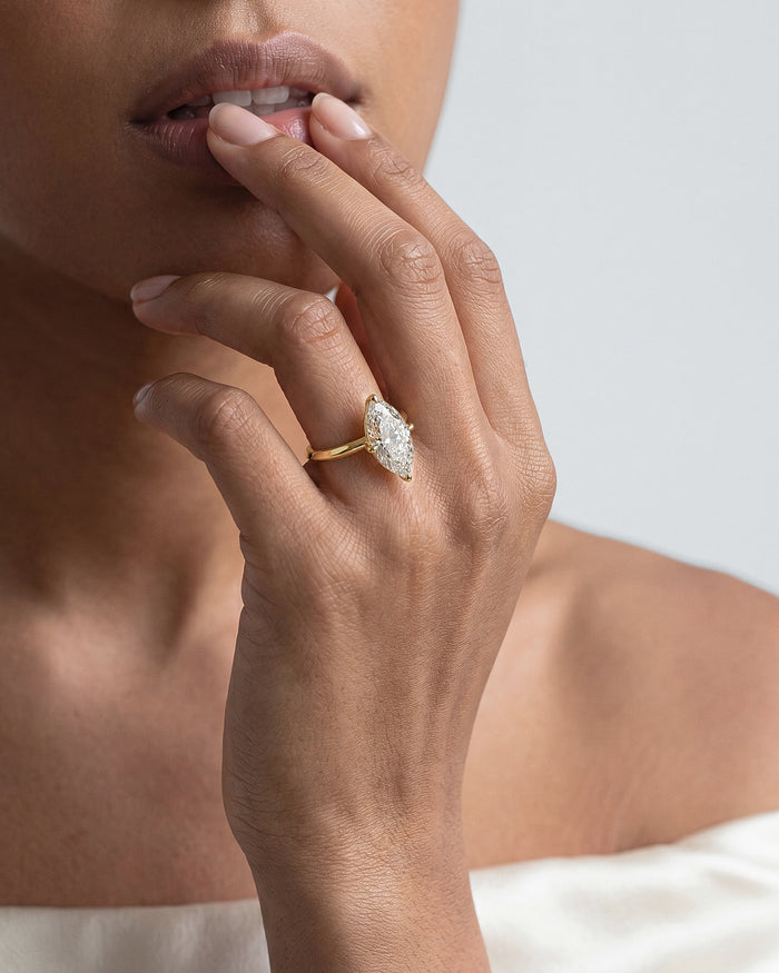Large marquise lab grown diamond statement solitaire in yellow gold worn on a hand raised to the lips
