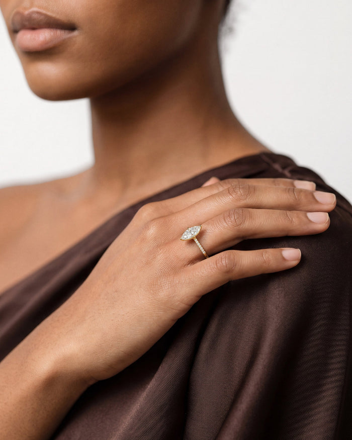 Large marquise lab grown diamond ring in yellow gold worn on a hand resting on a brown draped shoulder