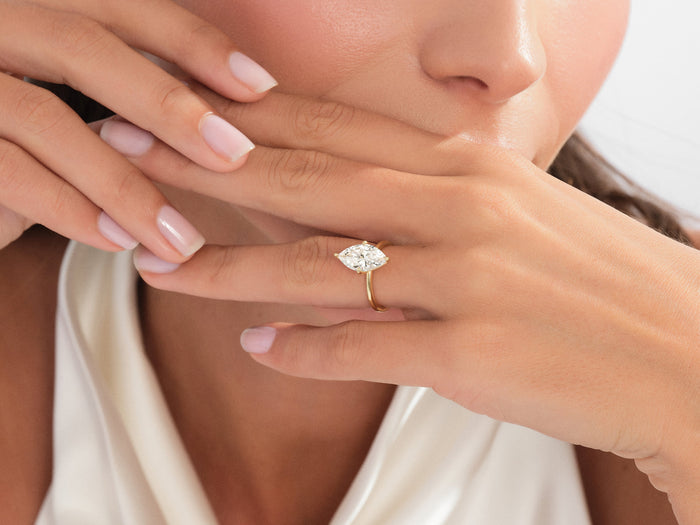 Marquise lab grown diamond solitaire in yellow gold worn with the fingers raised to the lips