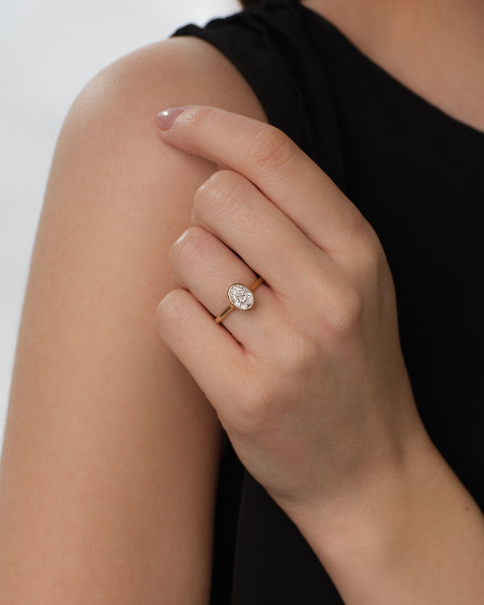 Oval lab grown diamond bezel solitaire in yellow gold worn on the hand resting on the shoulder