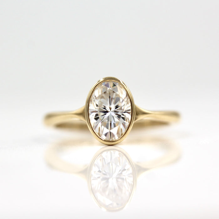 Oval cut moissanite bezel engagement ring on a pinched tapered yellow gold band