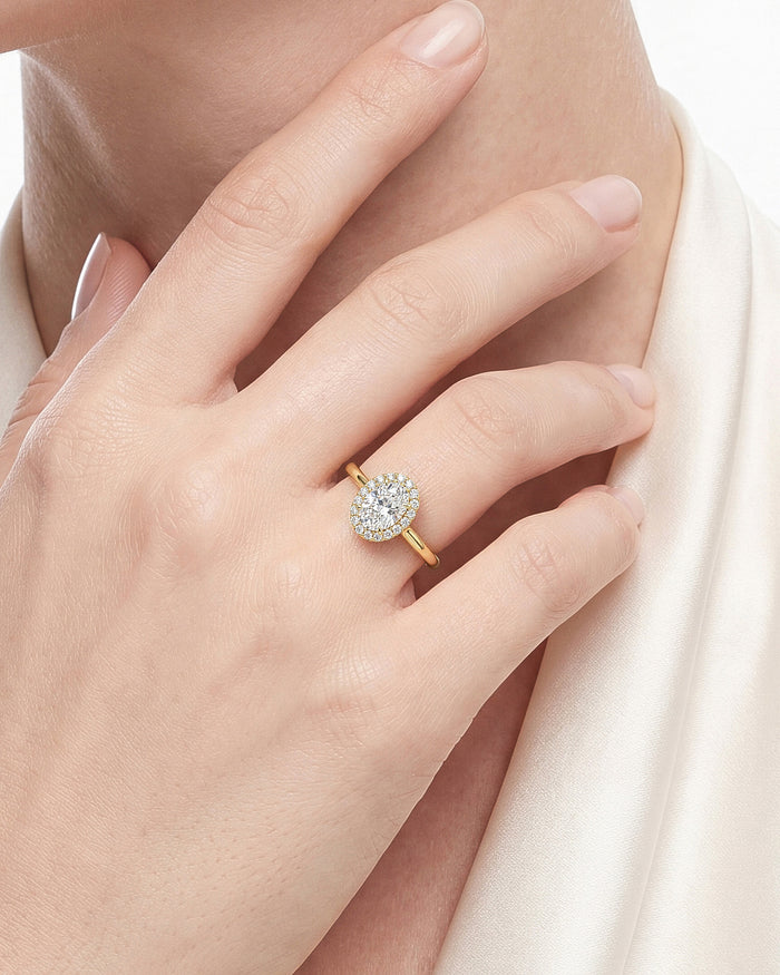 Oval cut moissanite halo ring in yellow gold worn on the hand near the neck