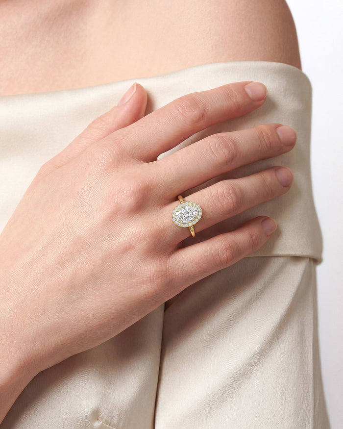 Oval moissanite halo ring in yellow gold worn on the hand against cream fabric
