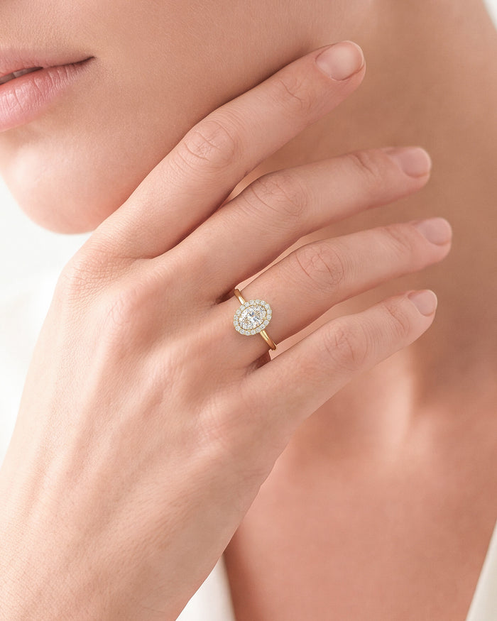 Dainty oval halo moissanite ring in yellow gold worn on a hand at the jaw