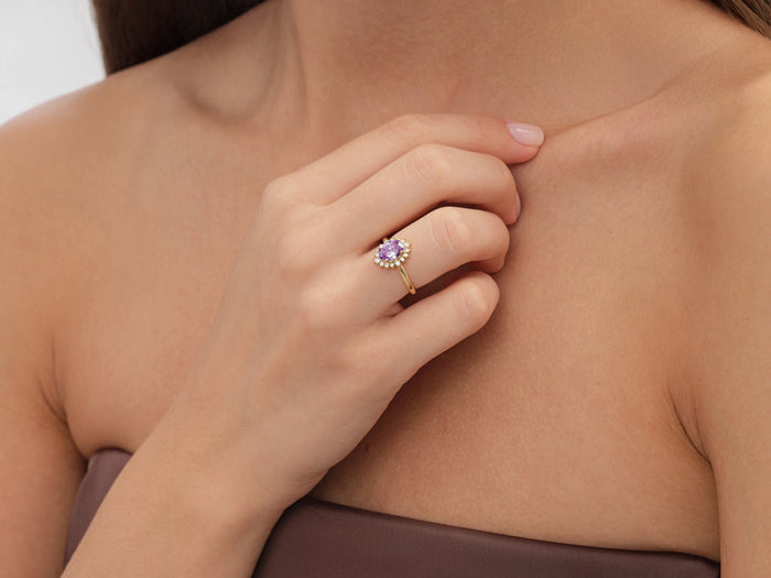 Oval cluster halo ring setting in yellow gold worn on the hand at the collarbone, lavender display stone