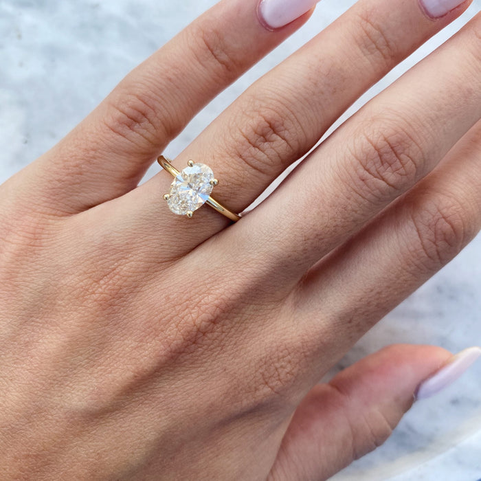 Oval cut moissanite double claw solitaire engagement ring on a fine yellow gold band, view 2