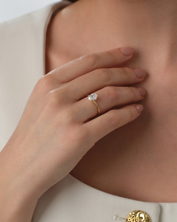 Oval moissanite four claw solitaire in yellow gold worn on the hand at the neckline