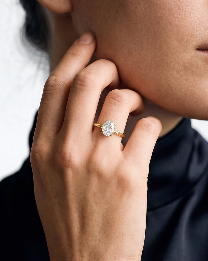 Oval lab grown diamond secret halo ring in yellow gold worn at the jaw with a black top