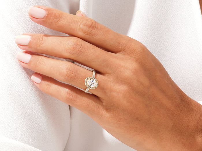 Oval cut lab grown diamond halo engagement ring worn on the hand resting on a white jacket