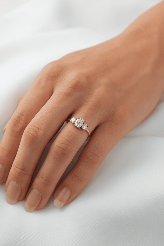Oval cut moissanite three stone engagement ring with large round side stones on a flat yellow gold band, view 2