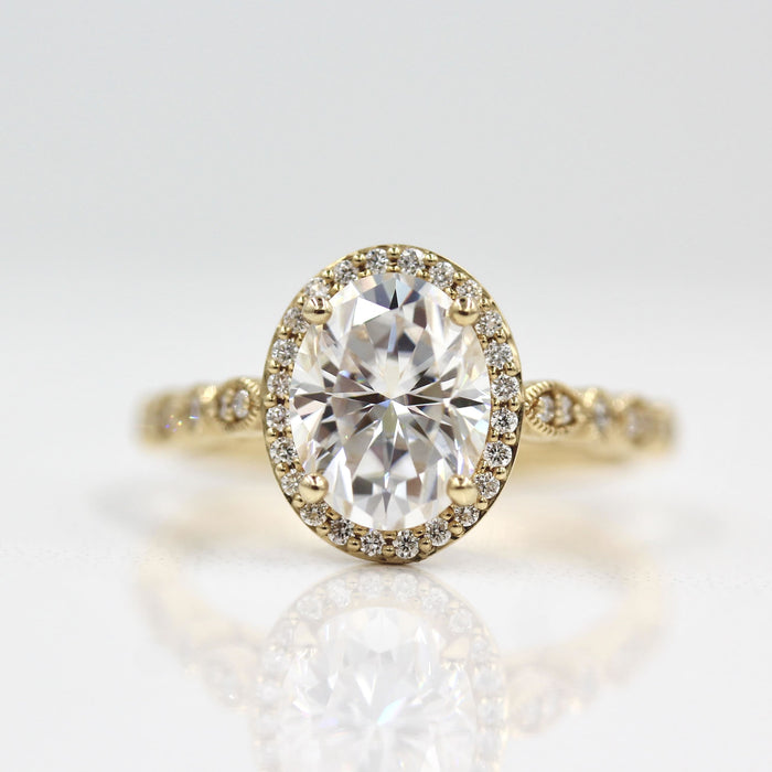 Oval cut moissanite halo engagement ring on a lobed milgrain band in yellow gold
