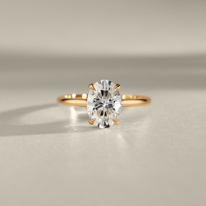 Oval cut moissanite pointed claw solitaire engagement ring on a rounded yellow gold band