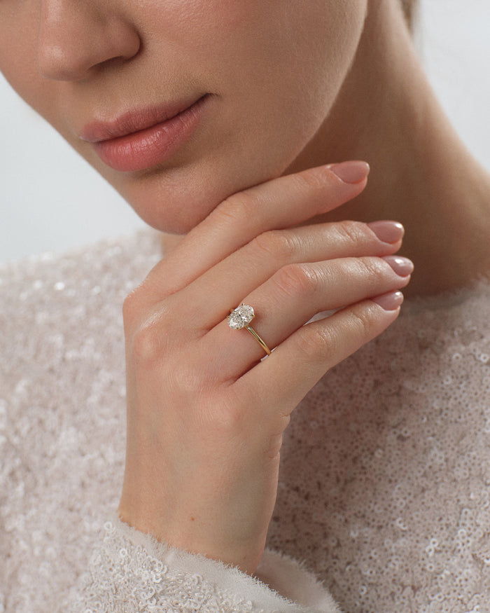 Oval moissanite solitaire engagement ring in gold worn on the hand, thin plain band