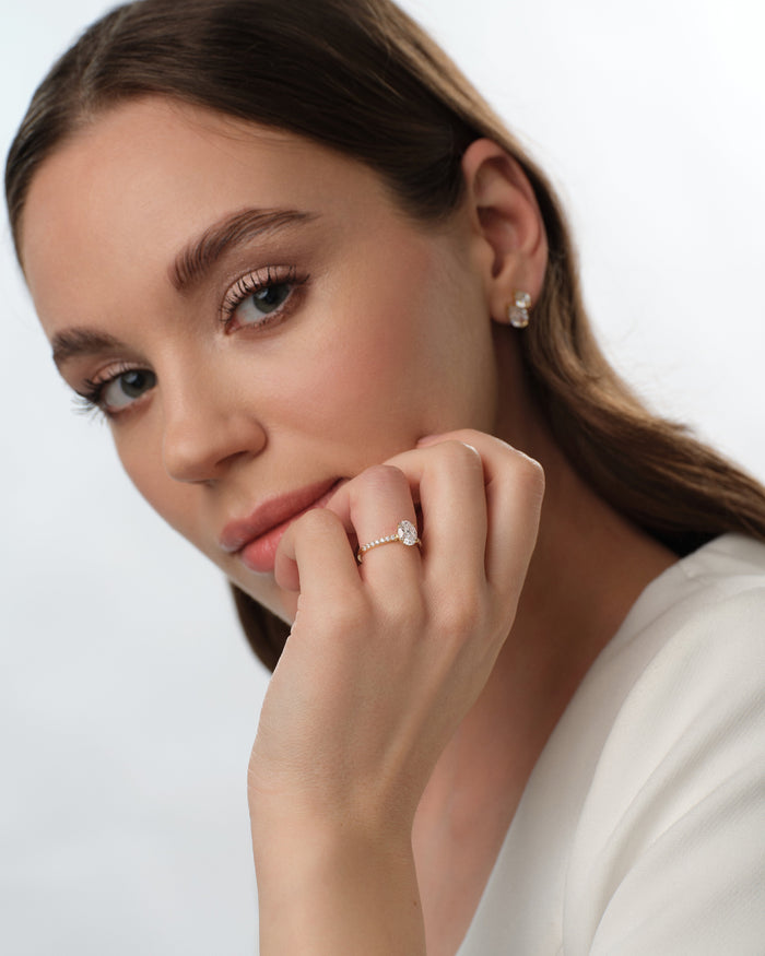 Oval lab grown diamond pave shoulder engagement ring worn on the hand held to the chin