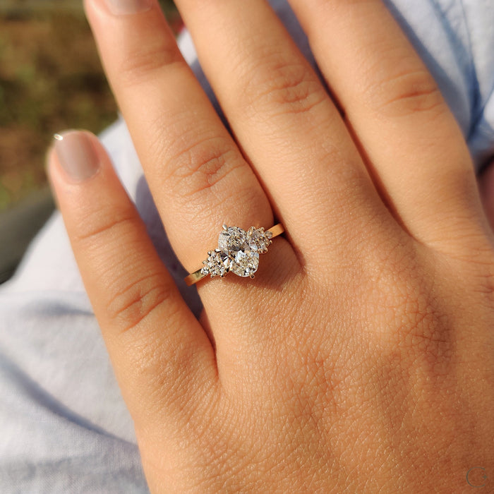 Oval cut moissanite trio cluster shoulder engagement ring on a flat yellow gold band, view 2