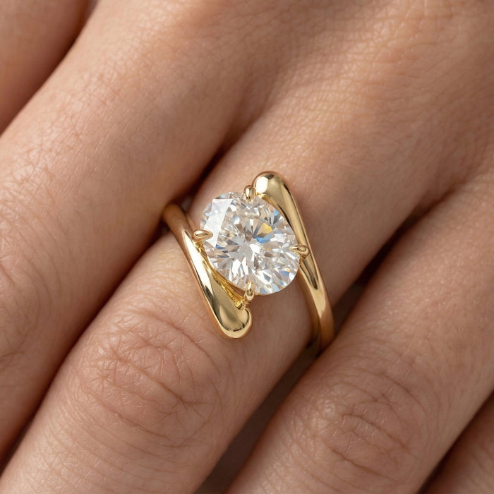 Oval cut moissanite held between two tapering gold tails in a swirl solitaire ring, view 2