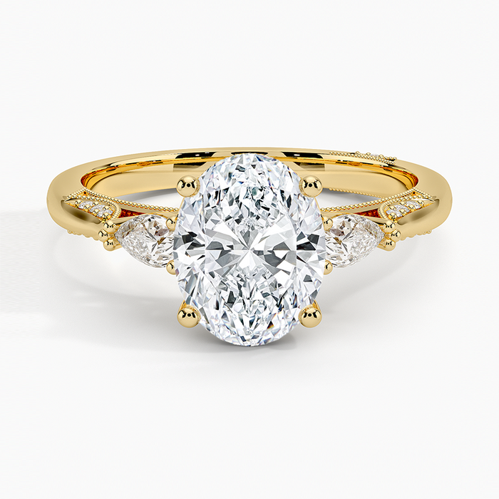 Oval moissanite with pear side stones and milgrain scroll wings in yellow gold, top view