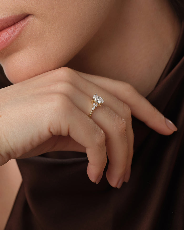 Vintage inspired oval lab grown diamond ring worn on the hand at the chin against brown silk