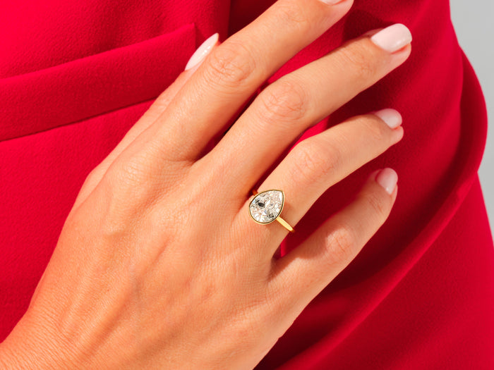 Large pear lab grown diamond bezel statement ring in yellow gold worn on the hand against red fabric