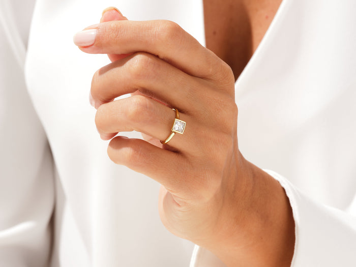 Princess lab grown diamond minimalist bezel ring in yellow gold on a hand held near the chest