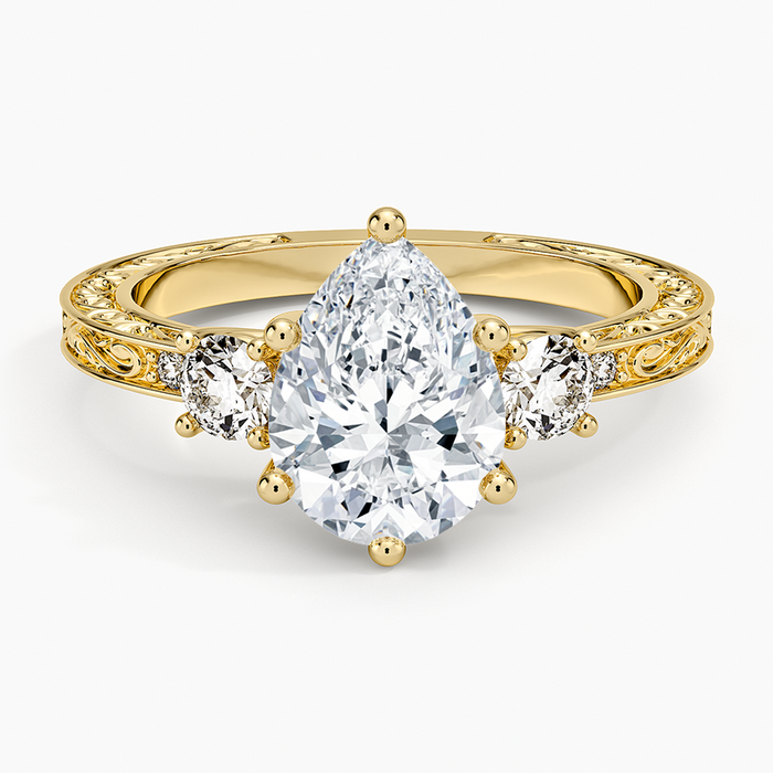 Pear cut moissanite hand engraved scroll three stone engagement ring in yellow gold, top view