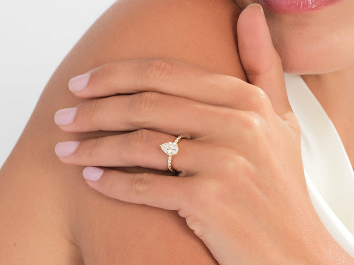 Pear moissanite pave band engagement ring in yellow gold worn on the hand resting on the shoulder