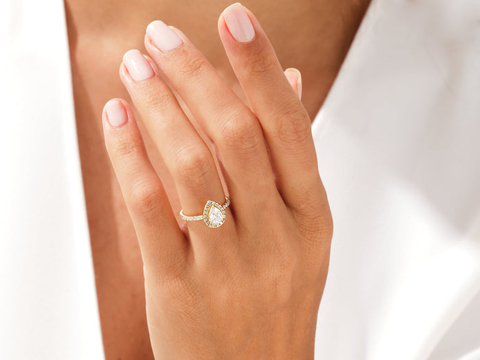Teardrop pear moissanite halo engagement ring in yellow gold worn on the hand