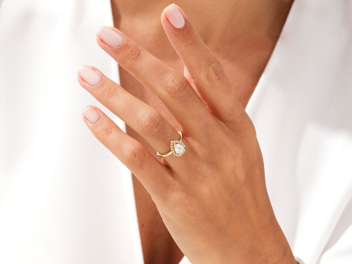 Dainty pear halo moissanite ring worn on a raised hand