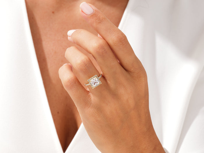 Square princess lab grown diamond halo ring in rose gold worn on the hand near the collar