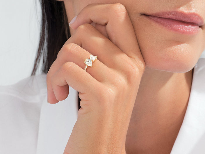 Heart and pear moissanite toi et moi ring in yellow gold worn on the hand at the chin