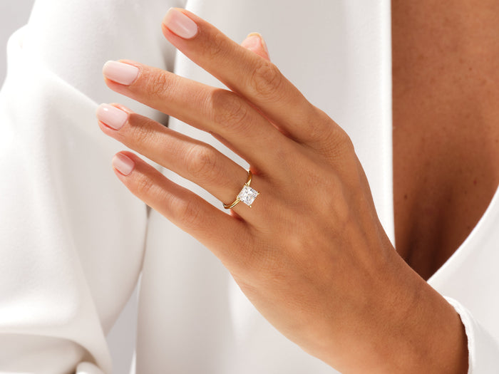 Princess cut lab grown diamond four claw ring on a relaxed hand against a white jacket