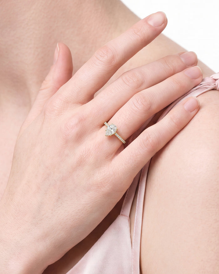 Pear shaped lab grown diamond ring worn on a hand resting on the shoulder over a pink slip