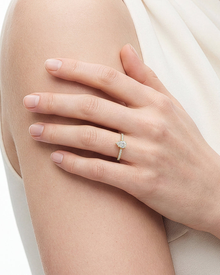 Dainty pear cut lab grown diamond ring in yellow gold on a hand holding the upper arm