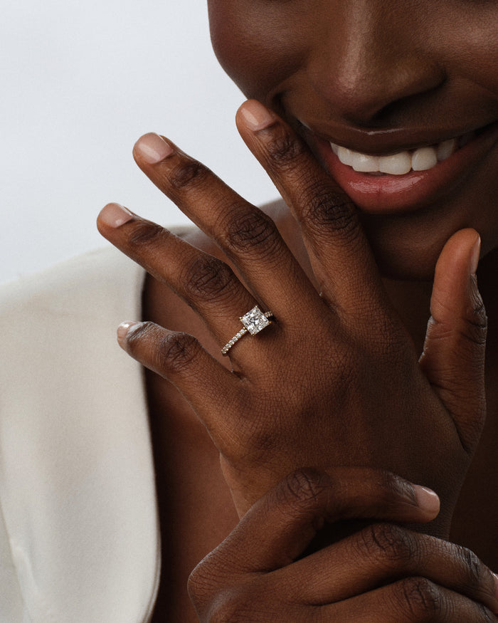Princess cut lab grown diamond micro pave engagement ring worn on the hand near a smile