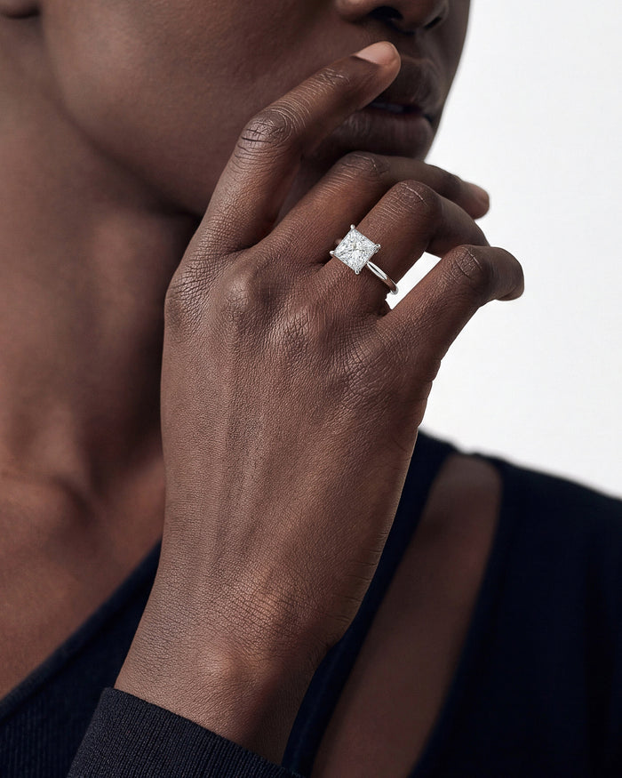 Large princess cut lab grown diamond solitaire in white gold worn on the hand near the lips