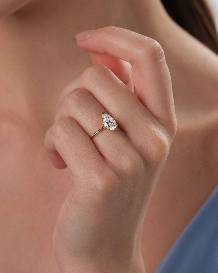 Pear shaped lab grown diamond solitaire in yellow gold on the hand held near the neck