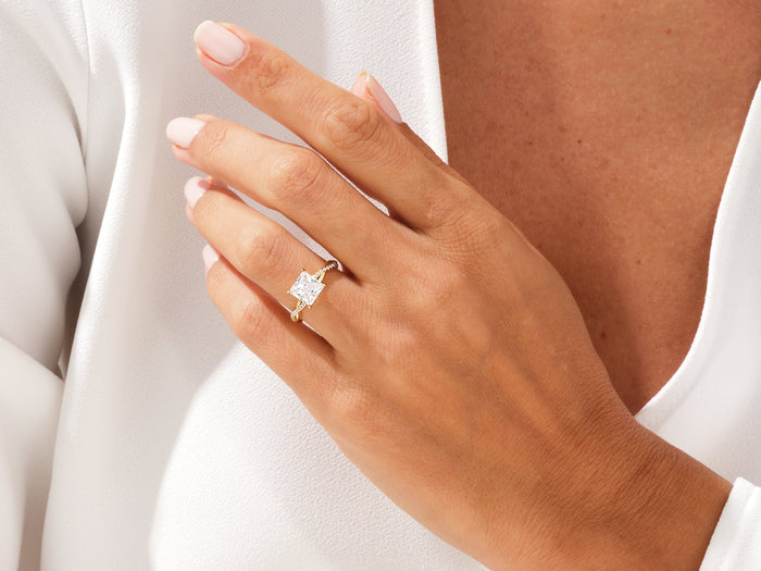 Princess cut lab grown diamond twisted engagement ring in yellow gold worn on the hand against a white blouse
