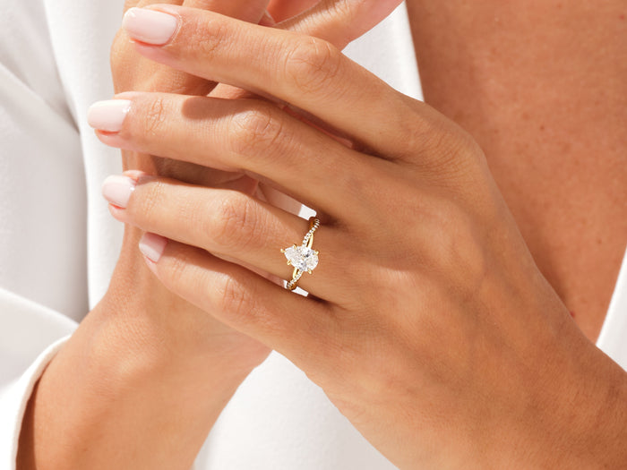 Pear shaped lab grown diamond infinity twist ring in yellow gold on a hand with fingers laced