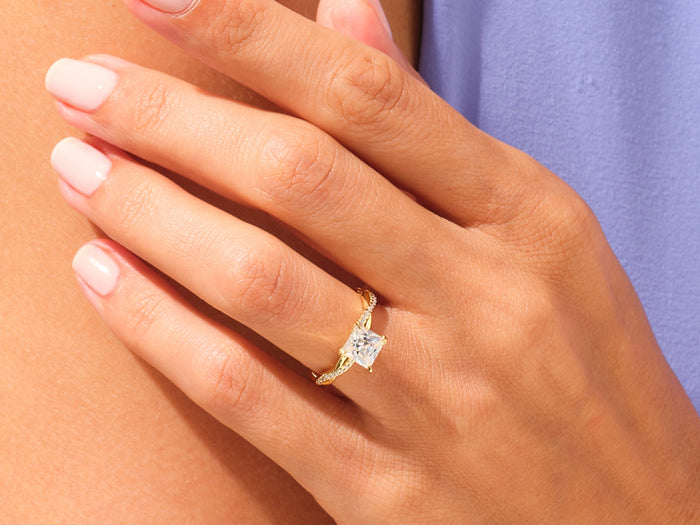 Large princess cut lab grown diamond rope twist ring in yellow gold worn on a hand at the shoulder, lilac background