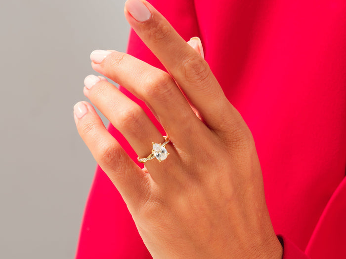 Large pear lab grown diamond crossover twist ring in yellow gold worn on the hand against a red sleeve